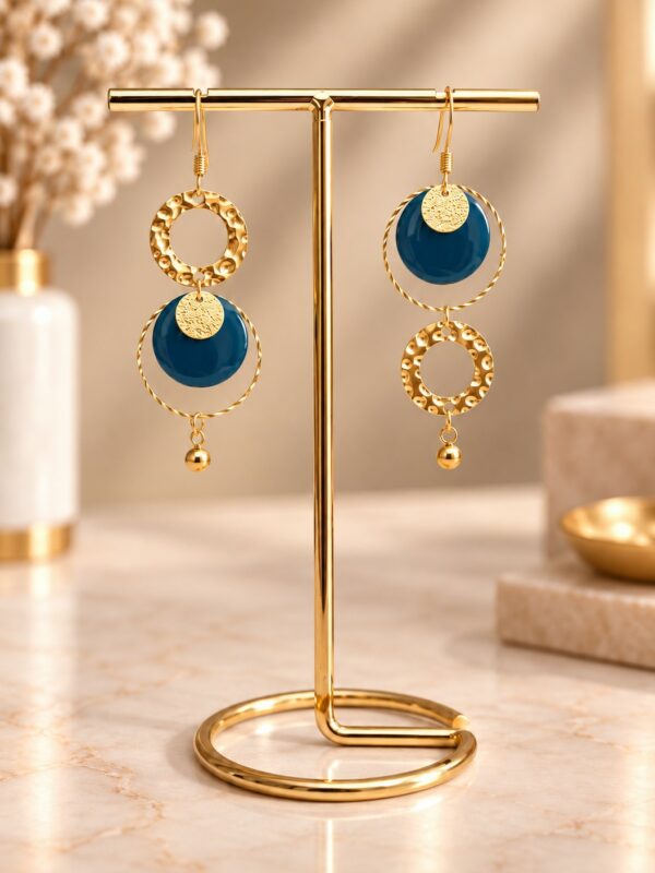 Boucles d'oreilles Nellie asymétriques dorées et bleu canard présentées sur support.