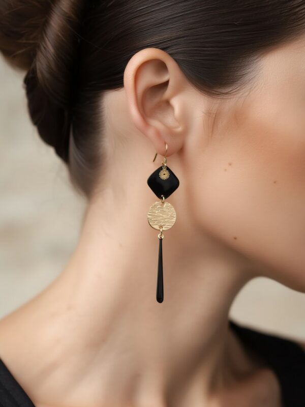 Boucles d'oreilles pendantes dorées et noires Adèle portées sur une oreille.