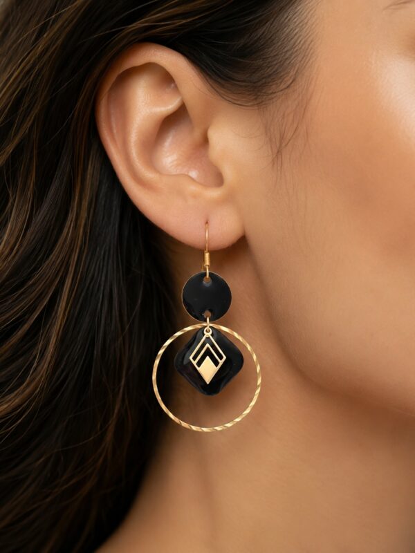 Boucles d'oreilles Adriana dorées et noires avec anneaux striés portées sur une oreille.