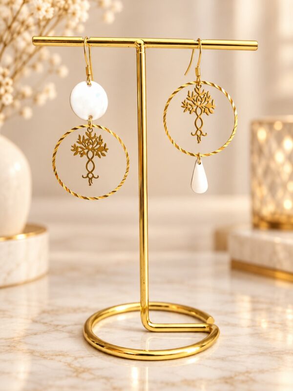 Boucles d'oreilles Agatha asymétriques dorées et blanches présentées sur support.