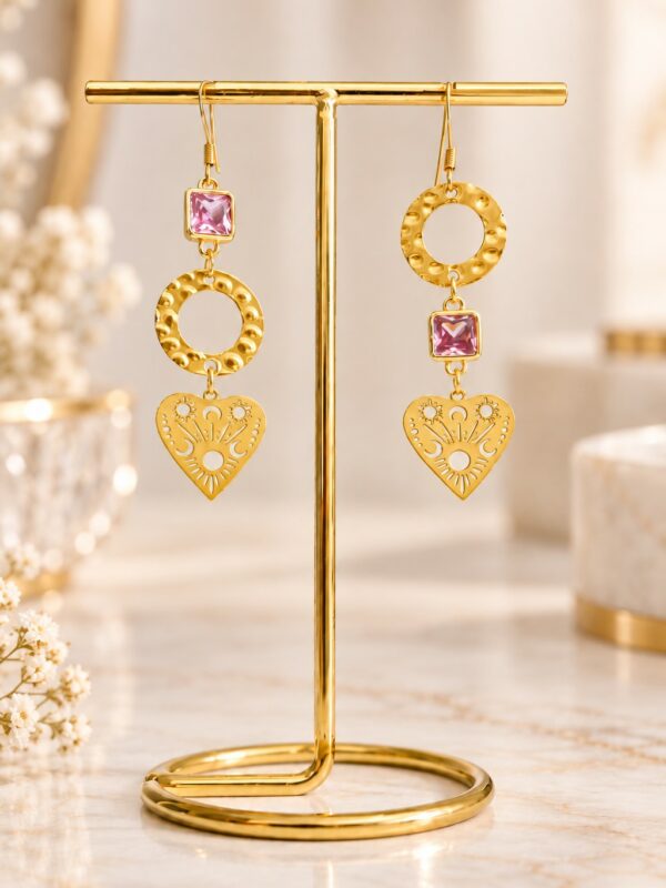 Boucles d'oreilles Aimée asymétriques dorées et roses présentées sur support.