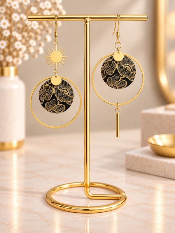 Boucles d'oreilles Angélina asymétriques dorées et noires présentées sur support.