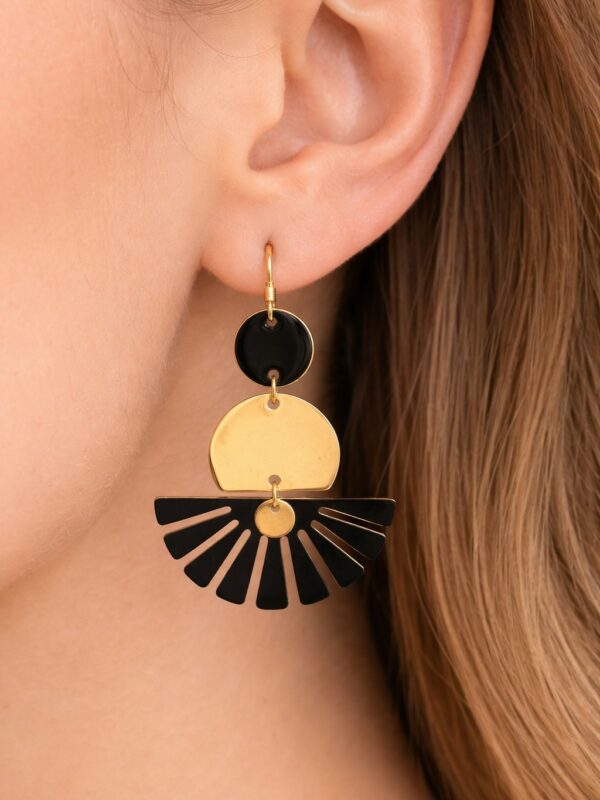 Boucles d'oreilles Charlize pendantes dorées et noires avec éventail portées sur une oreille.