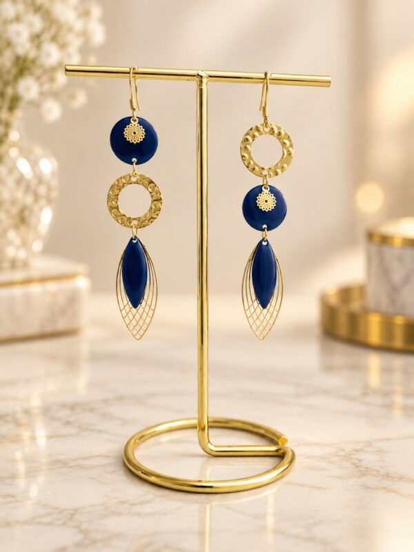 Boucles d'oreilles Charlotte asymétriques dorées et bleu nuit présentées sur support.