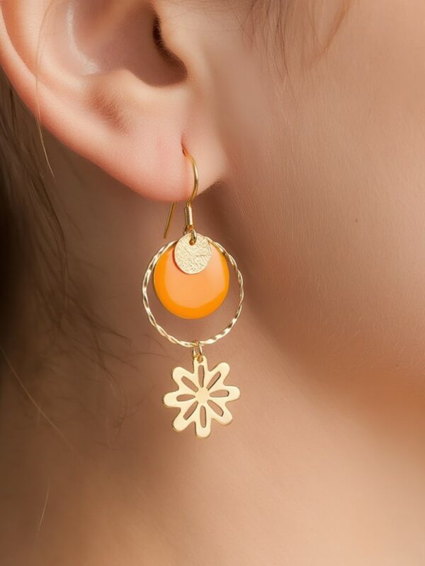 Boucles d'oreilles Flora pendantes dorées et orange motif fleur portées sur une oreille.