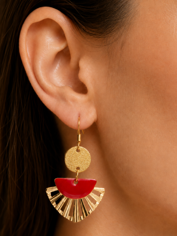 Boucles d'oreilles Garance pendantes dorées et rouges portées sur une oreille.