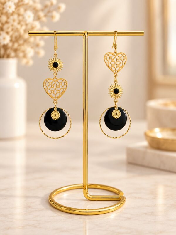 Boucles d'oreilles Kyra asymétriques dorées et noires présentées sur support.