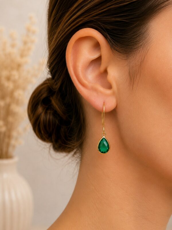 Boucles d'oreilles dorées perle en verre émeraude portées sur une oreille.