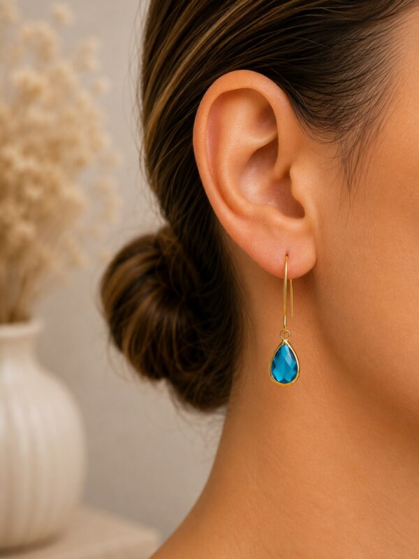 Boucles d'oreilles goutte bleue dorées Lili Marine portées sur une oreilles.