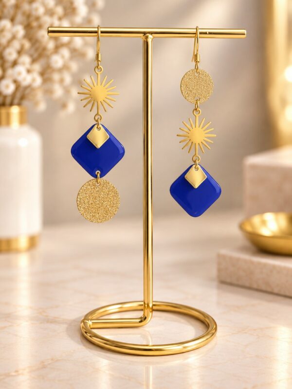 Boucles d'oreilles Marine asymétriques dorées et bleu roi présentées sur support.