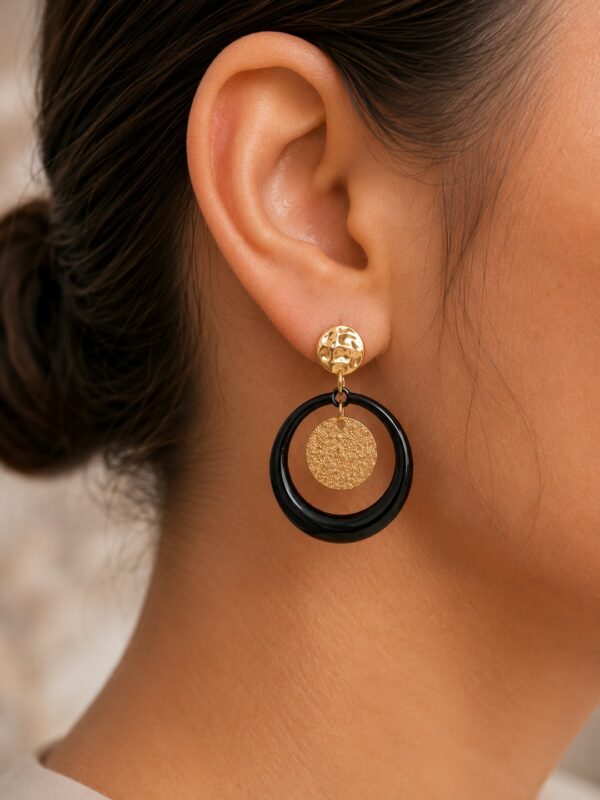 Boucles d'oreilles Maya dorées et noires portées sur une oreille.