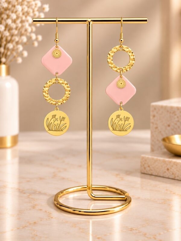Boucles d'oreilles Rosalie asymétriques dorées et roses présentées sur support.