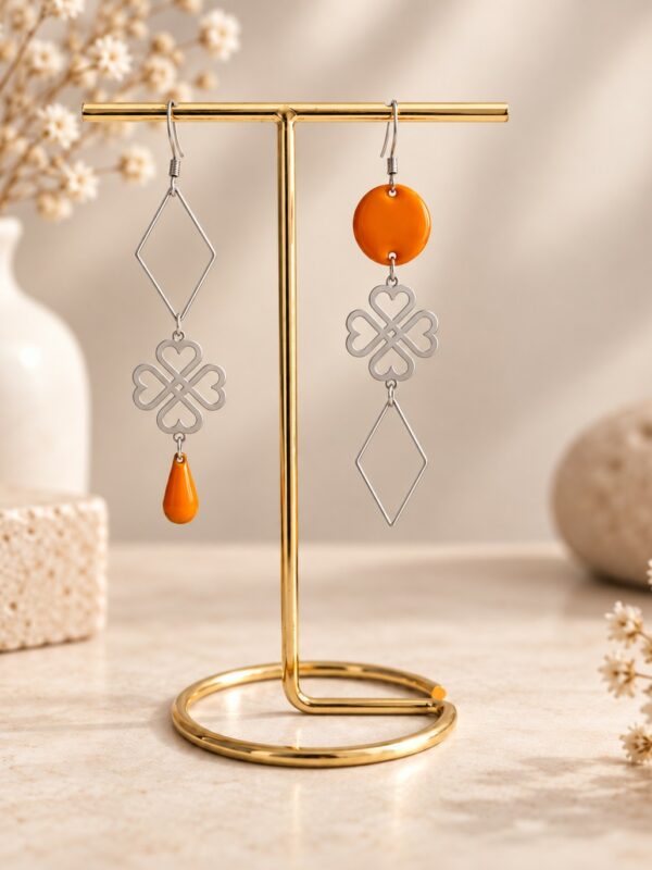 Boucles d'oreilles Seiko asymétriques argentées et orange présentées sur support.