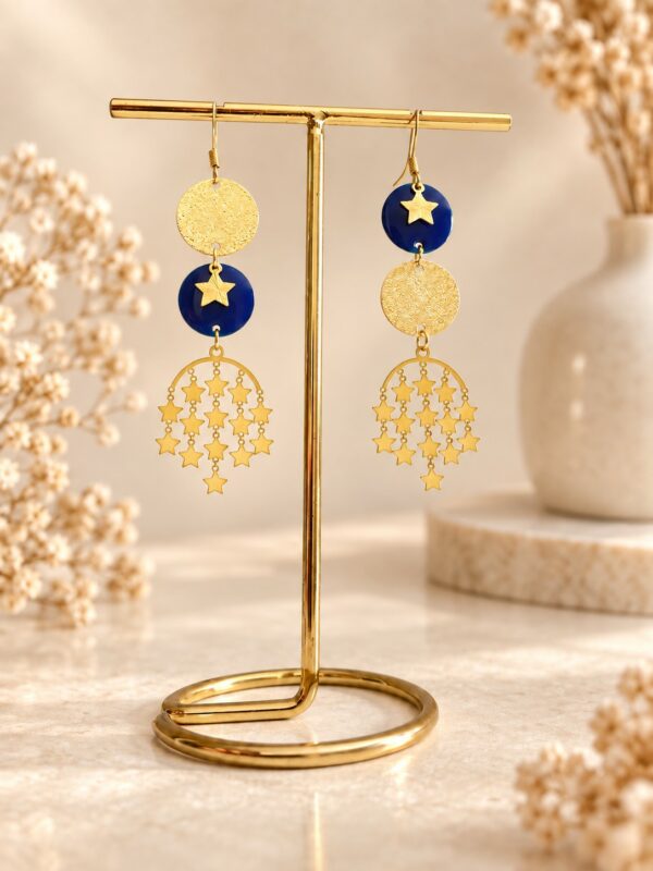 Boucles d'oreilles Stella asymétriques dorées et bleu nuit avec pluie d'étoiles sur support.