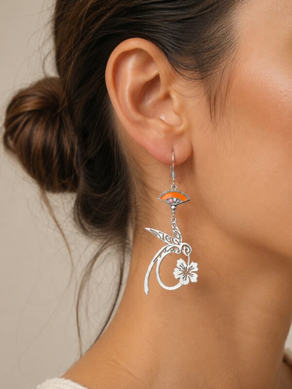 Boucles d'oreilles Colibri pendantes argentées et orange portées sur une oreille.