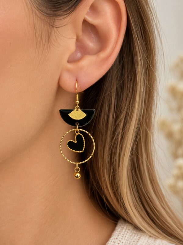 Boucles d'oreilles Lovely dorées et noires motif cœur portées sur une oreille.