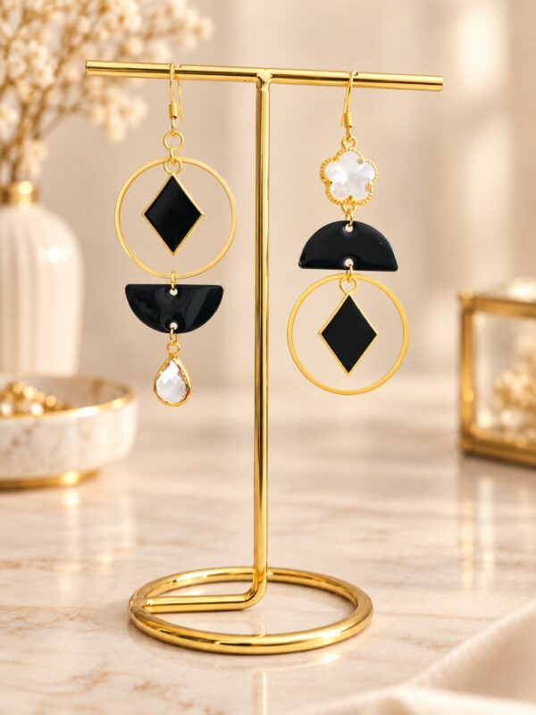 Boucles d'oreilles Millie asymétriques dorées et noires présentées sur support.