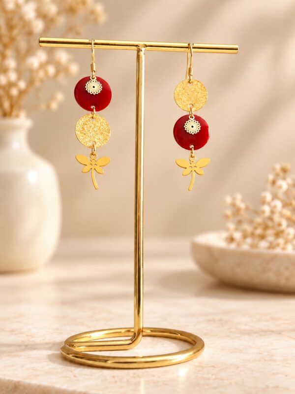 Boucles d'oreilles Sophia asymétriques dorées et bordeaux présentées sur support.