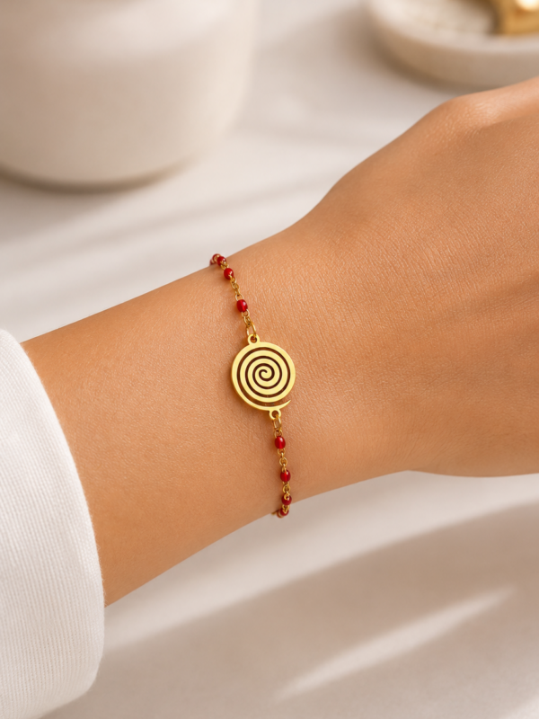 Bracelet doré et rouge en acier inoxydable porté au poignet avec médaillon spiralé doré et perles rouges - bracelet Andréa.