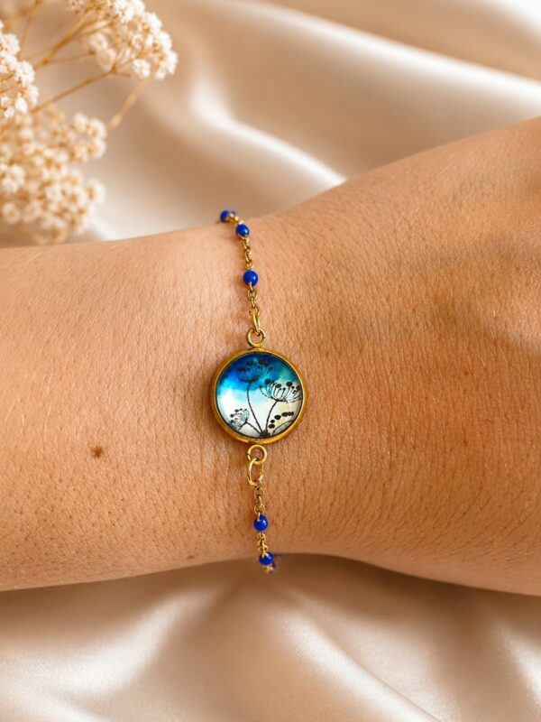 Bracelet doré et bleu en acier inoxydable avec médaillon fleuri porté au poignet