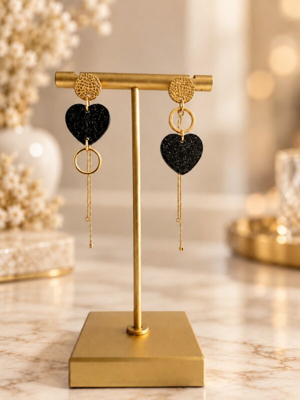 Boucles d'oreilles Amara asymétriques dorées et noir pailleté présentées sur support.