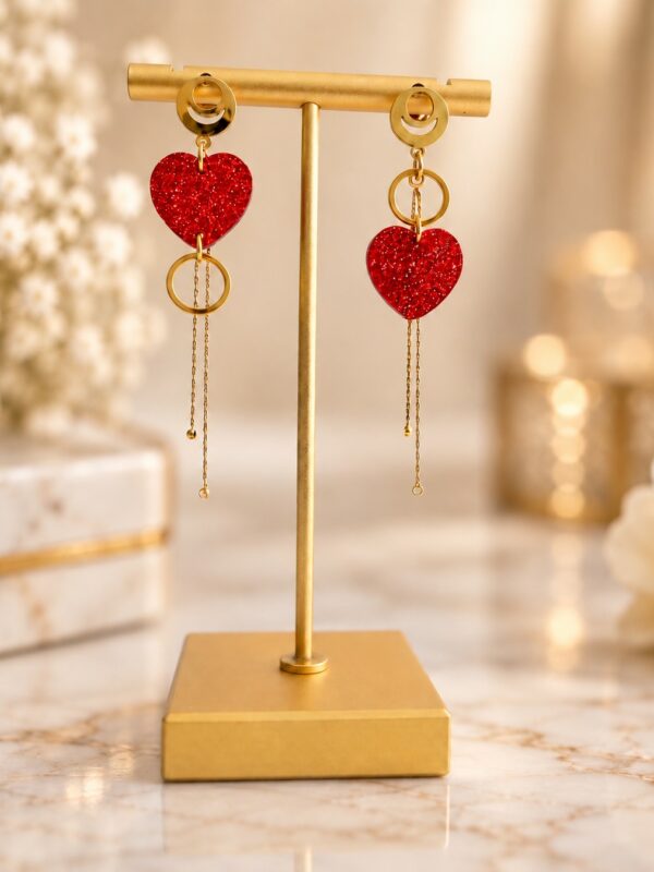 Boucles d'oreilles Esmée asymétriques dorées et rouge pailleté présentées sur support.