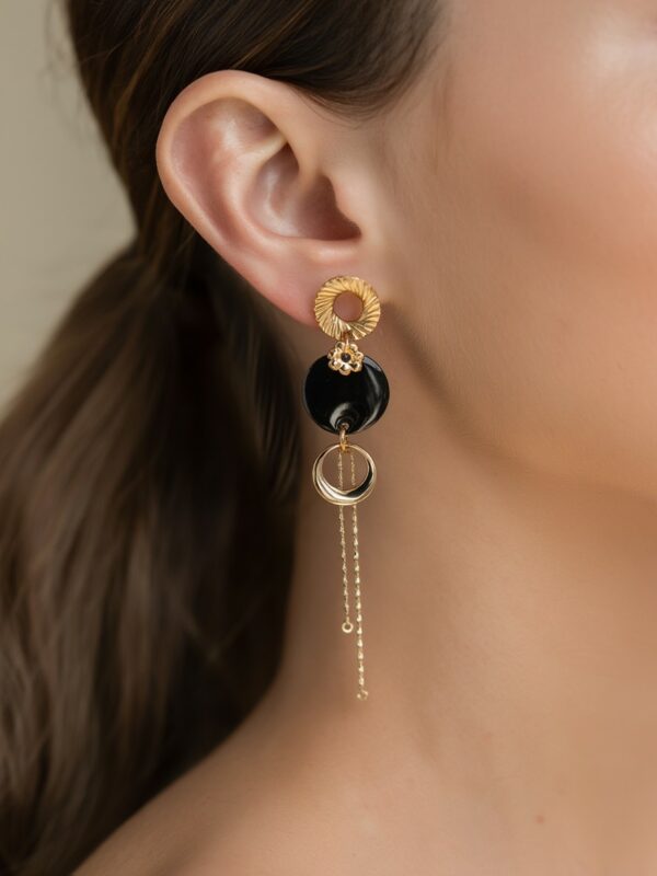 Boucles d'oreilles Héléna pendantes dorées et noires portées sur une oreille.