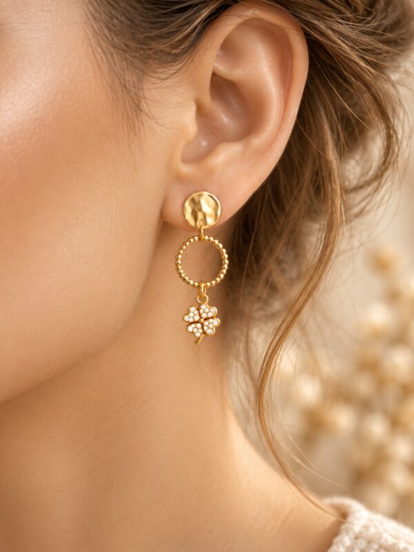 Boucles d'oreilles Olga dorées trèfle avec strass portées sur une oreille.