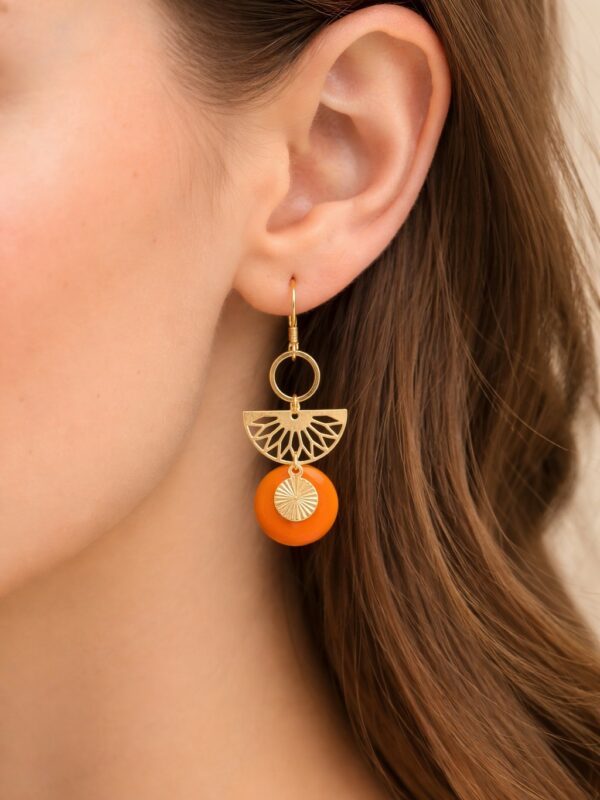 Boucles d'oreilles Lavinia pendantes dorées et orange portées sur une oreille.
