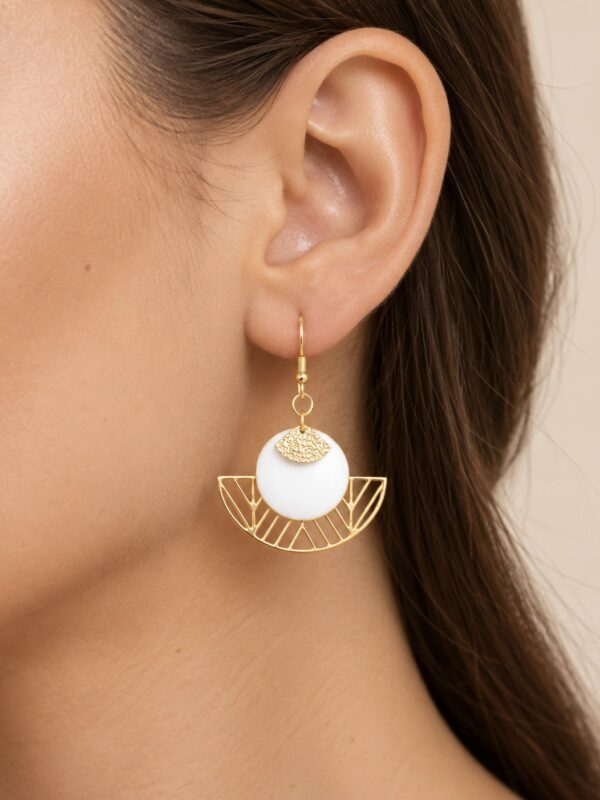 Boucles d'oreilles Wendy dorées et blanches portées sur une oreille.