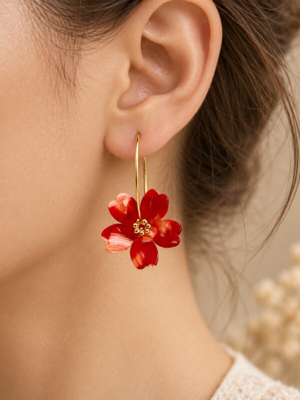 Créoles Thaïs dorées avec fleur rouge portées sur une oreille.