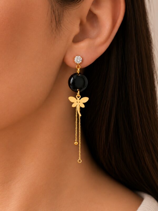 Boucles d'oreilles Victoria dorées et noires libellule portées sur une oreille.