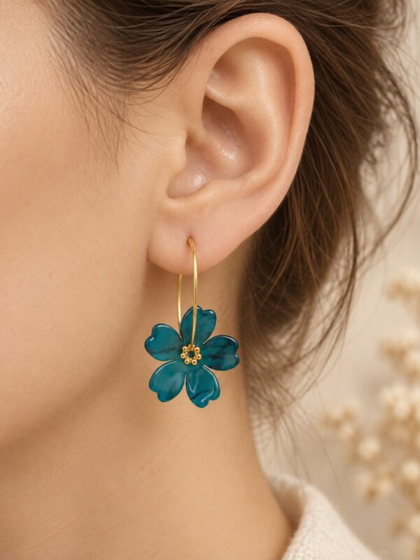 Créoles Iris dorées avec fleur bleu canard portées sur une oreille.