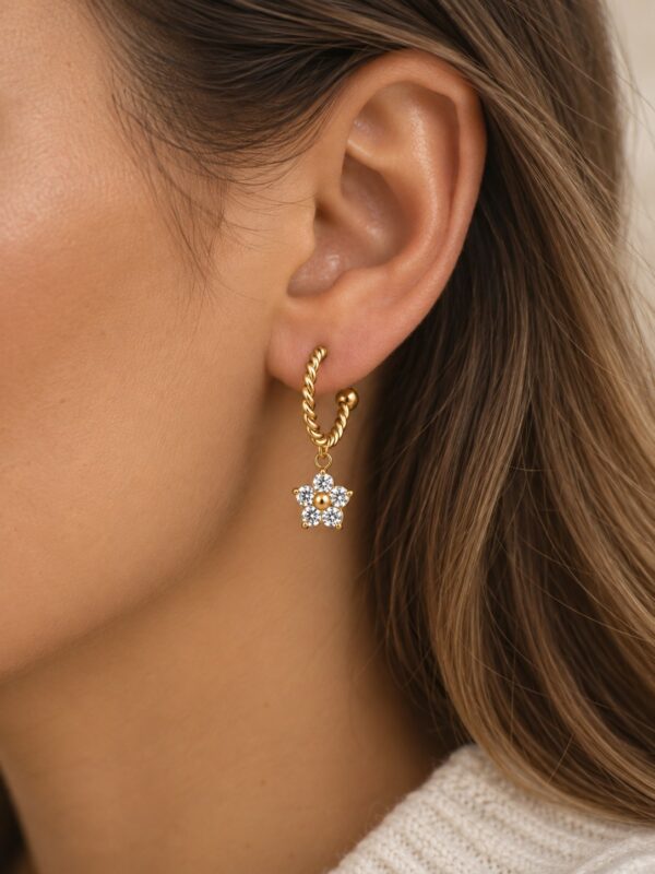 Créole Angélina semi-ouverte torsadée dorée avec fleur en zircone portée sur une oreille.