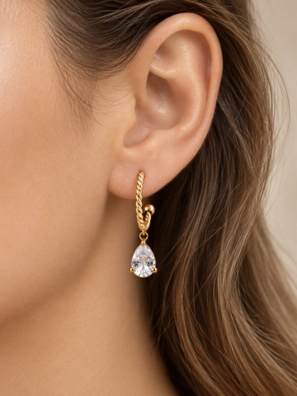 Créole Julia dorée semi-ouverte torsadée avec pendentif goutte en zircone portée sur une oreille.